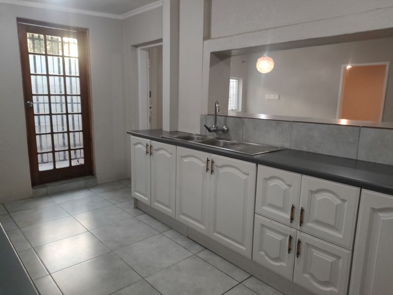 A functional kitchen featuring white cabinetry, a double sink with mixer tap, tiled flooring, and a timber-framed glass door leading to the exterior.
