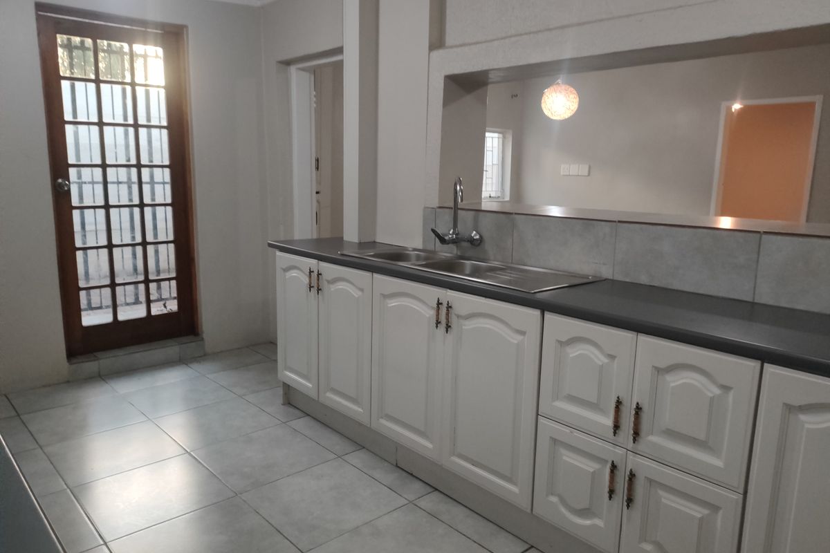 A functional kitchen featuring white cabinetry, a double sink with mixer tap, tiled flooring, and a timber-framed glass door leading to the exterior.