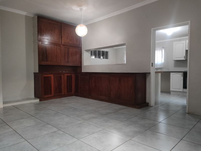 An empty living area featuring built-in wooden cabinetry, ceramic floor tiles, and a convenient pass-through window connecting to the kitchen.