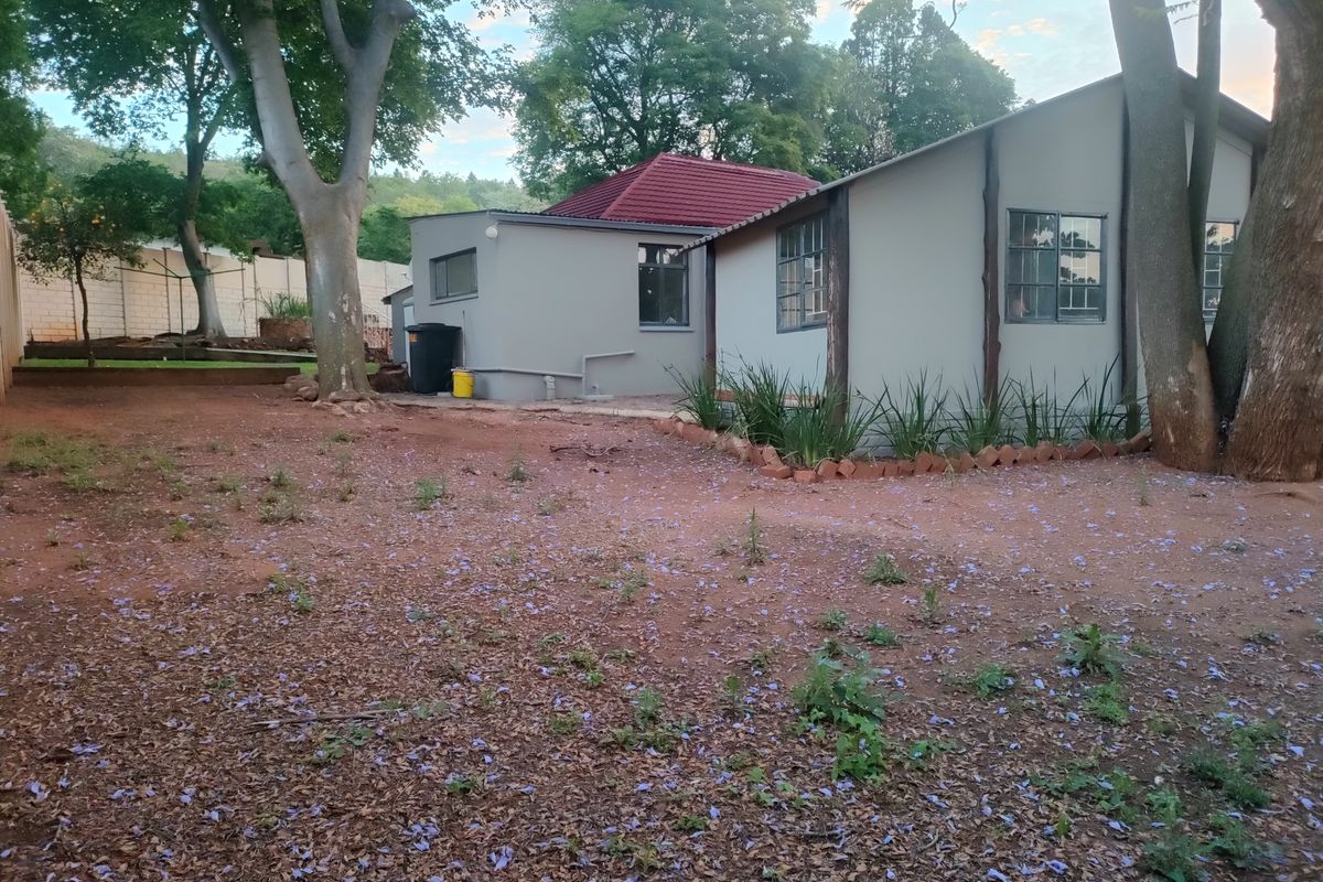 Rear view of the property showing the building exterior, tiled roof, steel-framed windows, and a large garden area with mature trees.