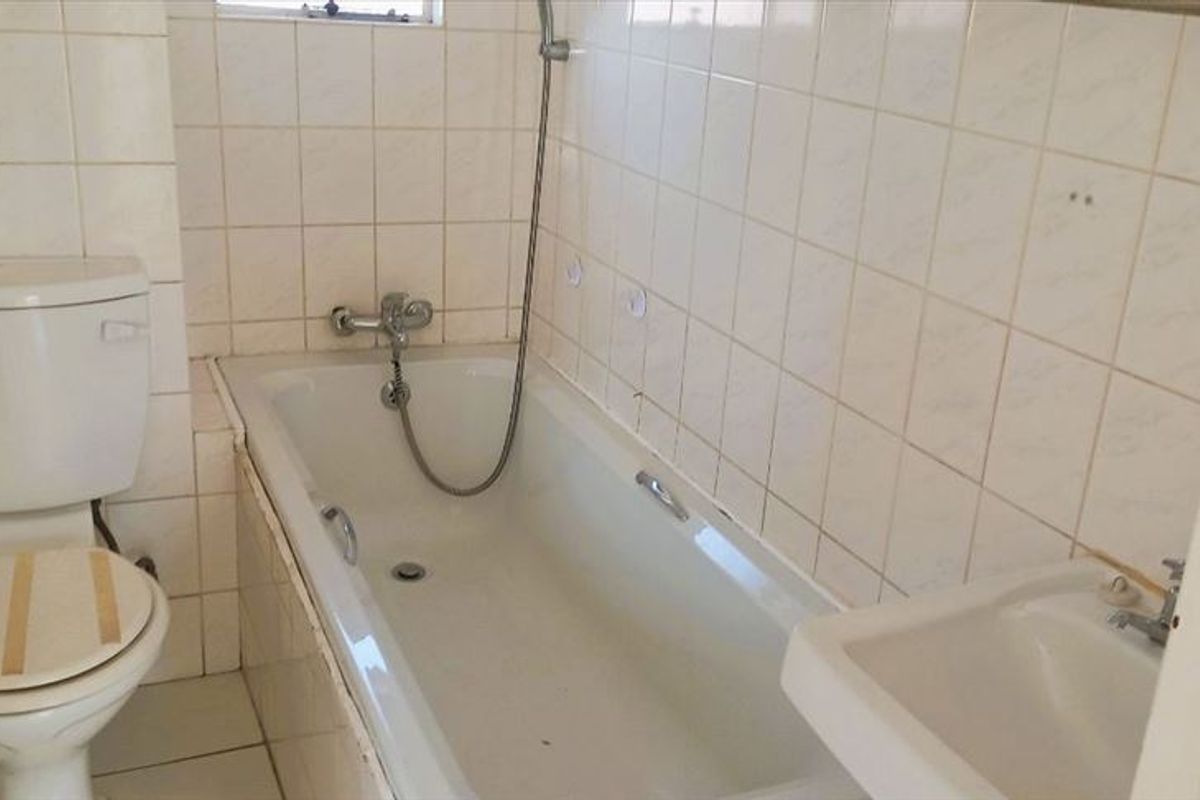 A dated bathroom featuring a standard bathtub with shower mixer, toilet, and basin, finished with wall and floor tiling.
