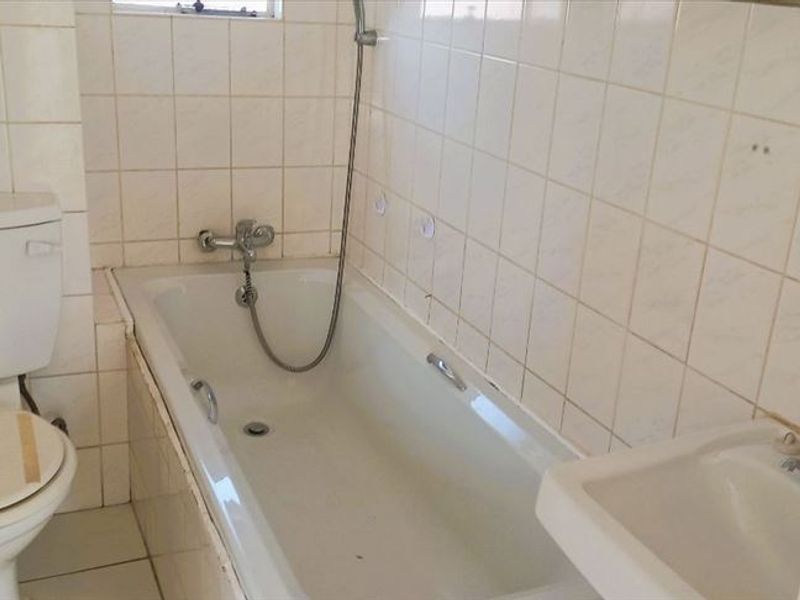 A dated bathroom featuring a standard bathtub with shower mixer, toilet, and basin, finished with wall and floor tiling.