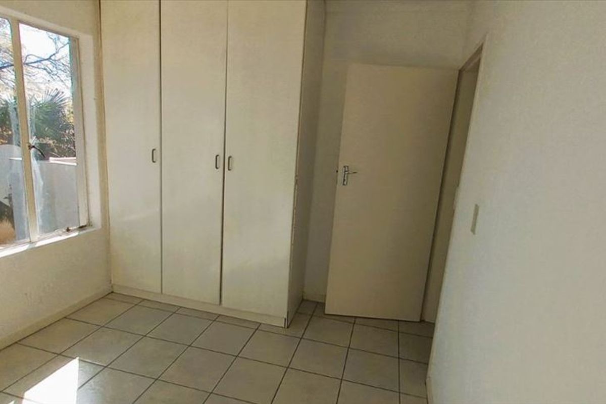 A bright, empty bedroom featuring tiled flooring and built-in cupboards, offering a clean canvas for personalization.