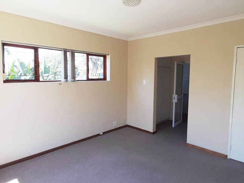 An empty bedroom featuring carpeted flooring, neutral walls, and windows fitted with security burglar bars.