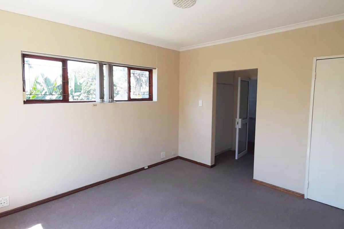 An empty bedroom featuring carpeted flooring, neutral walls, and windows fitted with security burglar bars.
