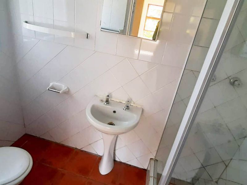 A functional bathroom featuring a pedestal basin, toilet, and a glass-enclosed shower with tiled finishes.