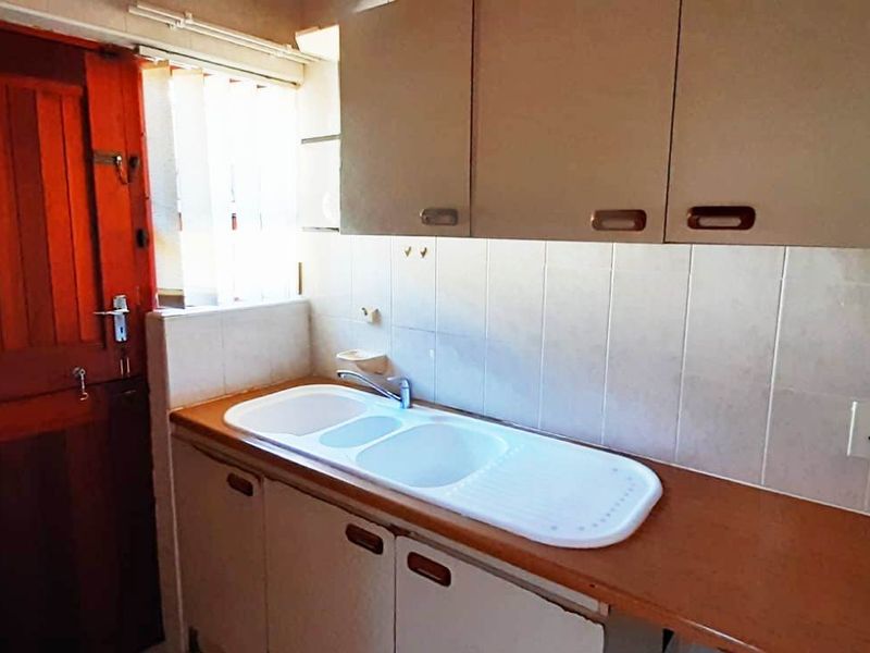 A functional scullery area featuring built-in cabinetry, a laminate countertop with a drop-in sink, and tiled splashbacks, providing practical utility space.