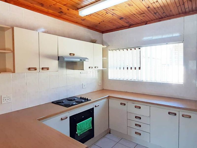 Functional kitchen featuring built-in cabinetry, laminate countertops, integrated electric hob, oven, and extractor fan, finished with a timber ceiling and tiled splashback.