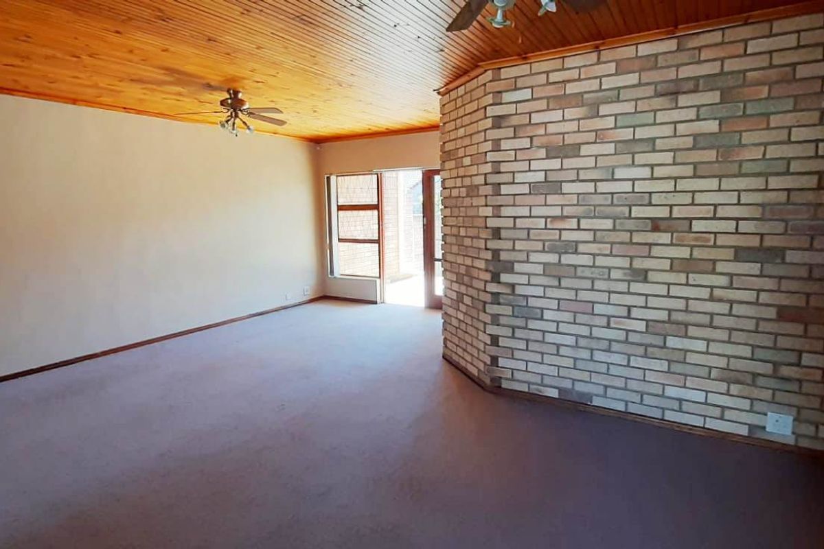 Spacious living area featuring a prominent brick feature wall, exposed timber ceiling, and direct access to the outdoor area through a sliding glass door.