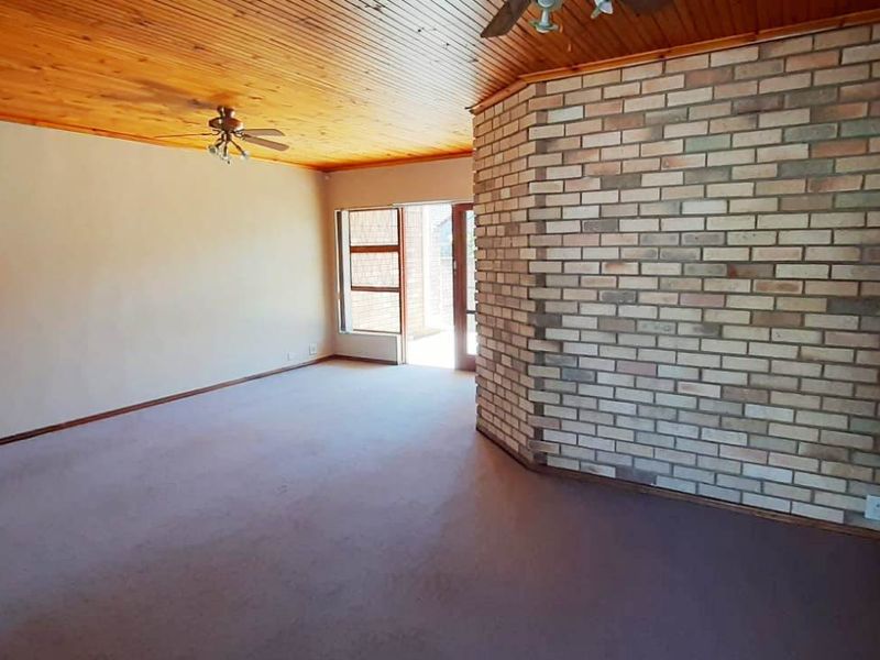 Spacious living area featuring a prominent brick feature wall, exposed timber ceiling, and direct access to the outdoor area through a sliding glass door.