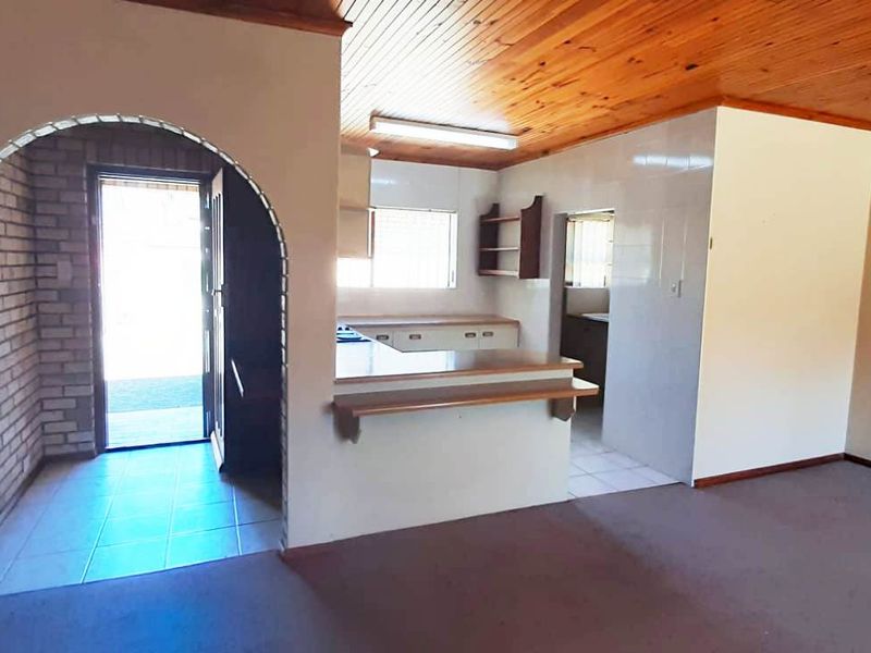 Open plan living area featuring a timber ceiling, brick archway, and a functional kitchen layout with a breakfast bar.