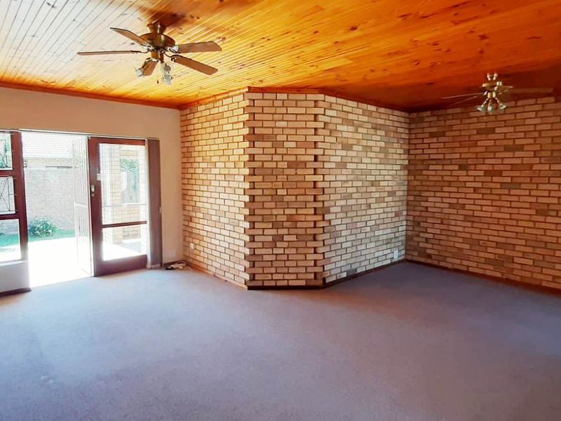 Spacious living area featuring an exposed timber ceiling, brick feature walls, and direct access to the outdoor patio through sliding glass doors.