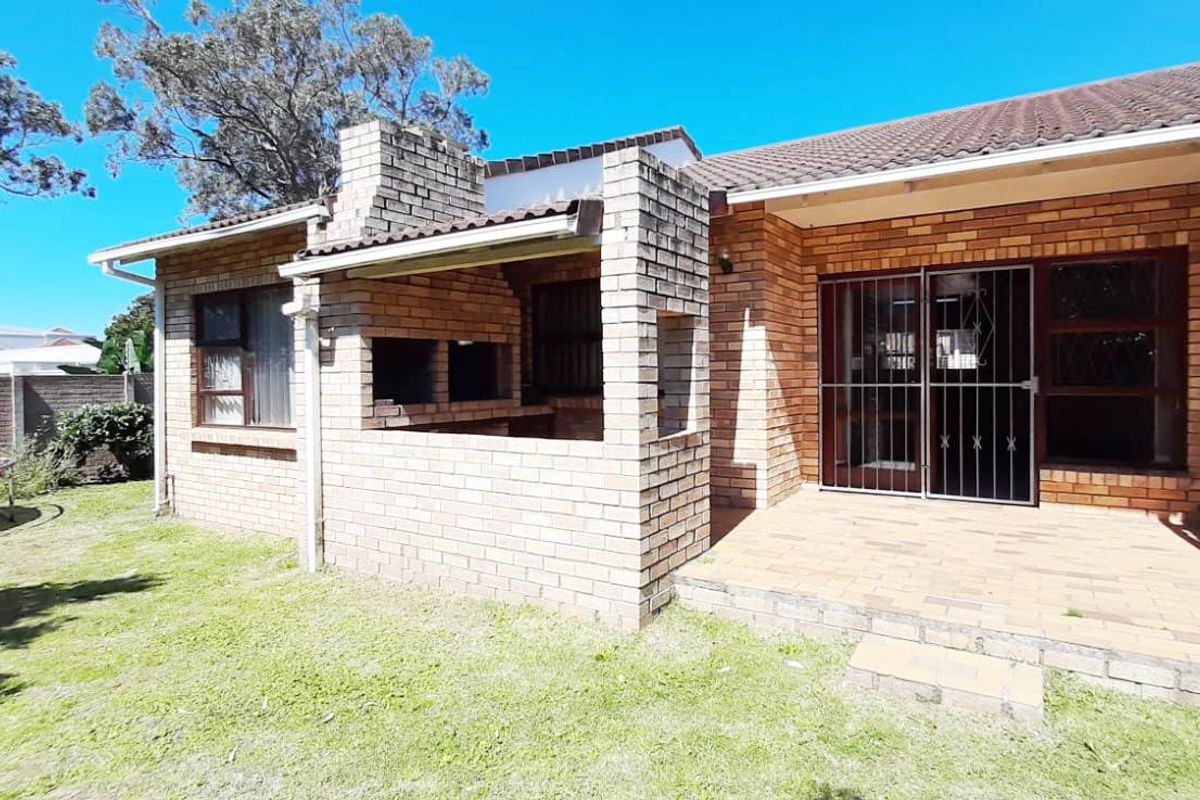 Rear exterior view of the townhouse featuring a paved patio area and a built-in brick braai, set against a private garden space.