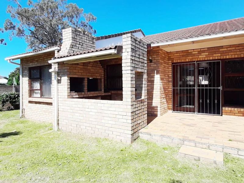 Rear exterior view of the townhouse featuring a paved patio area and a built-in brick braai, set against a private garden space.