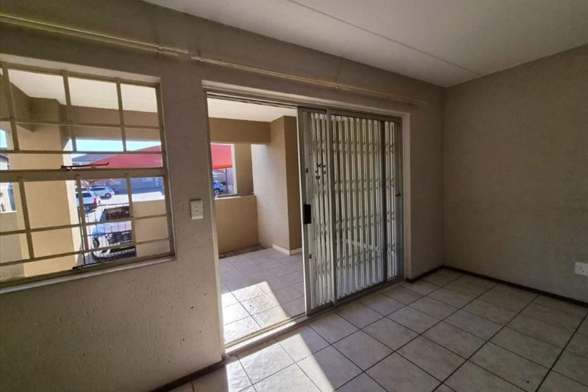 An empty living area featuring tiled flooring, a sliding door with a security gate, and access to an outdoor patio space.
