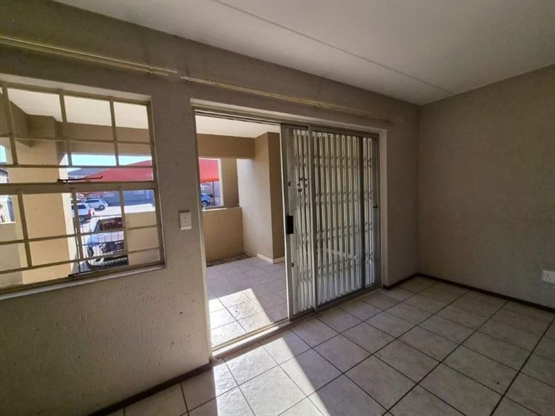An empty living area featuring tiled flooring, a sliding door with a security gate, and access to an outdoor patio space.