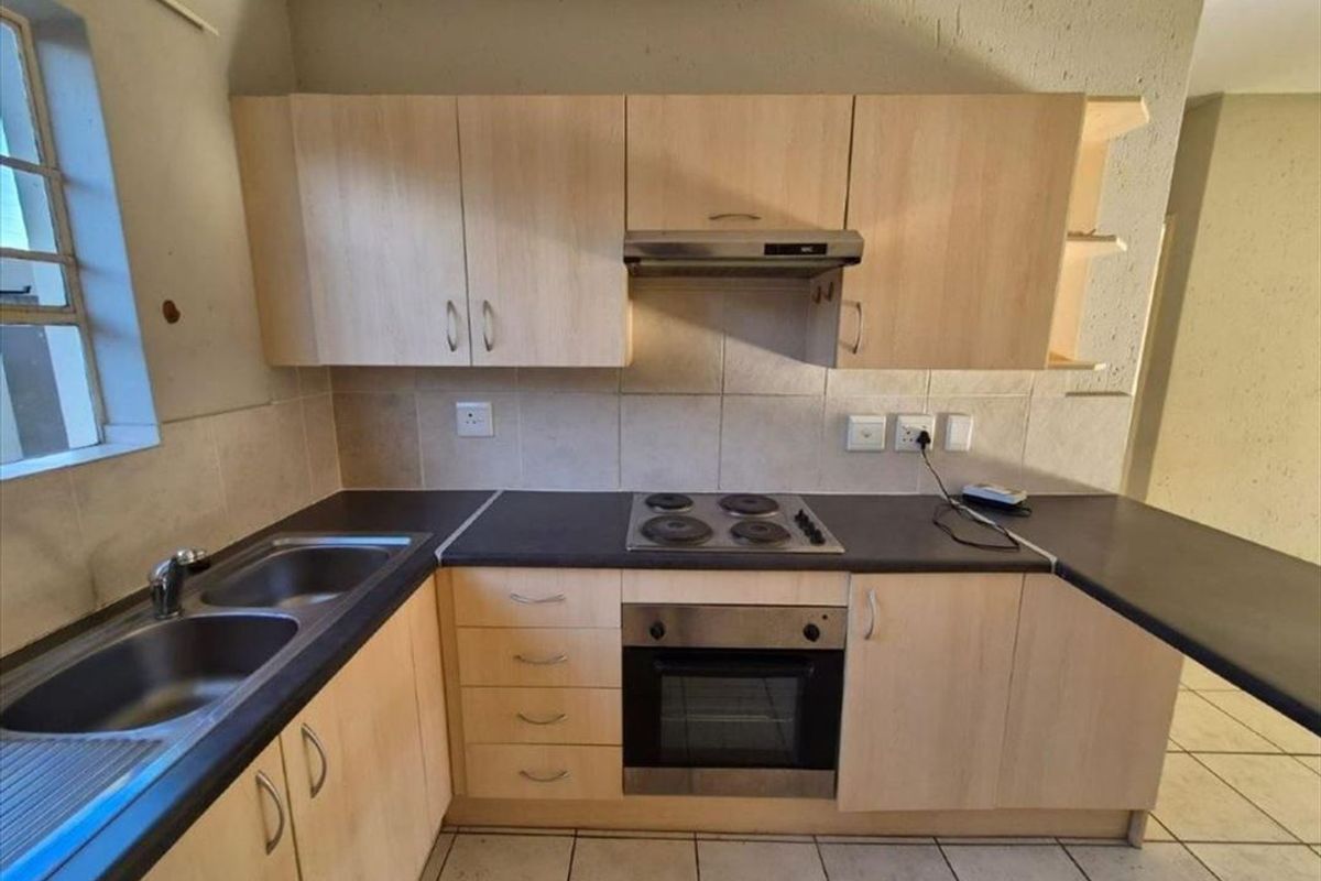 A functional kitchen featuring light wood-finish cabinetry, dark laminate countertops, a built-in oven, electric hob, and a stainless steel double sink.