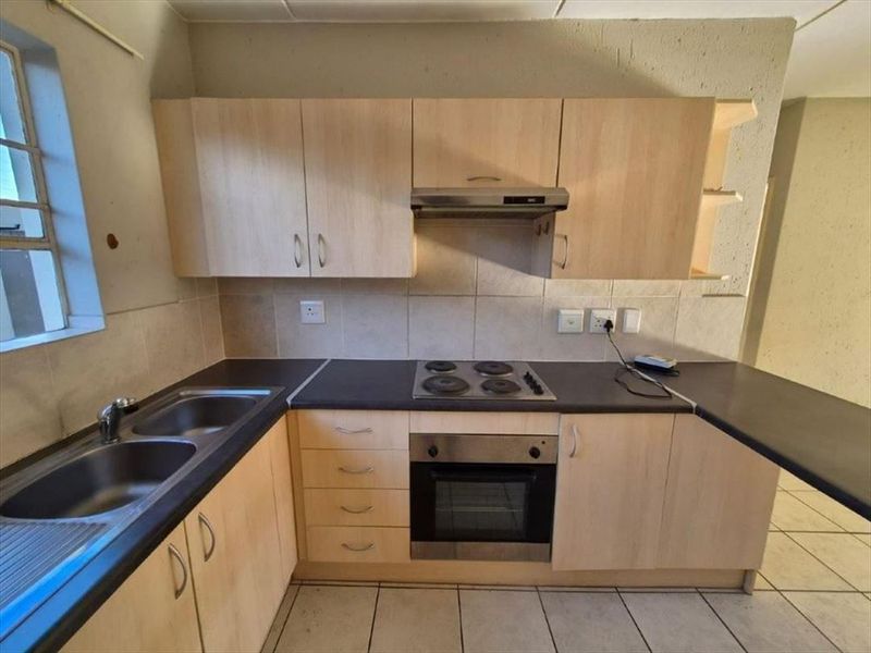 A functional kitchen featuring light wood-finish cabinetry, dark laminate countertops, a built-in oven, electric hob, and a stainless steel double sink.