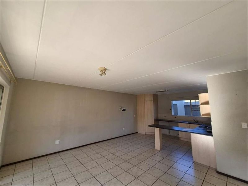 An open-plan living and kitchen area featuring tiled flooring, built-in cabinetry, and a breakfast bar, offering a blank canvas for potential renovation.