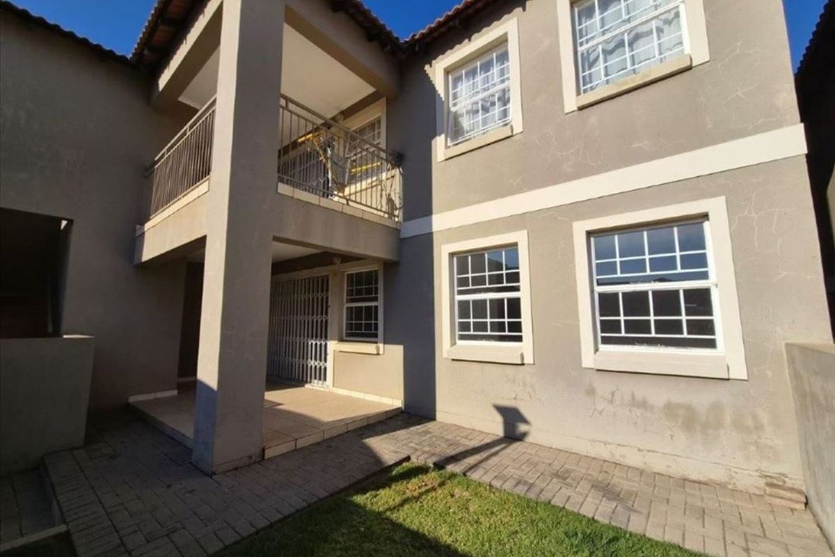 Rear view of the townhouse featuring a paved patio area, an upper-level balcony with metal railings, and a small garden space.