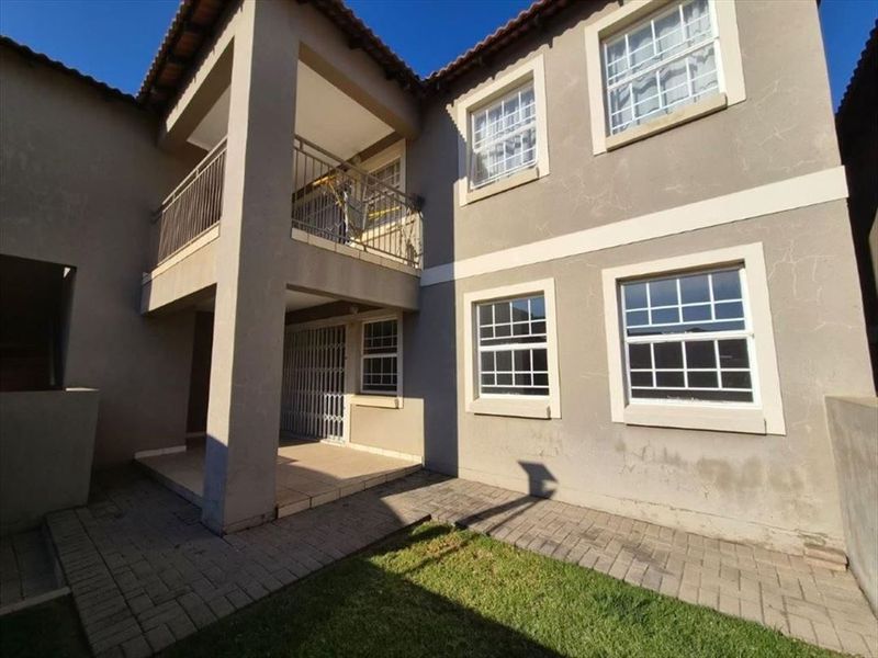 Rear view of the townhouse featuring a paved patio area, an upper-level balcony with metal railings, and a small garden space.
