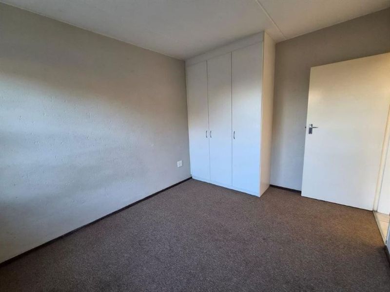 A clean, empty bedroom featuring neutral wall finishes, carpeted flooring, and a functional built-in wardrobe.