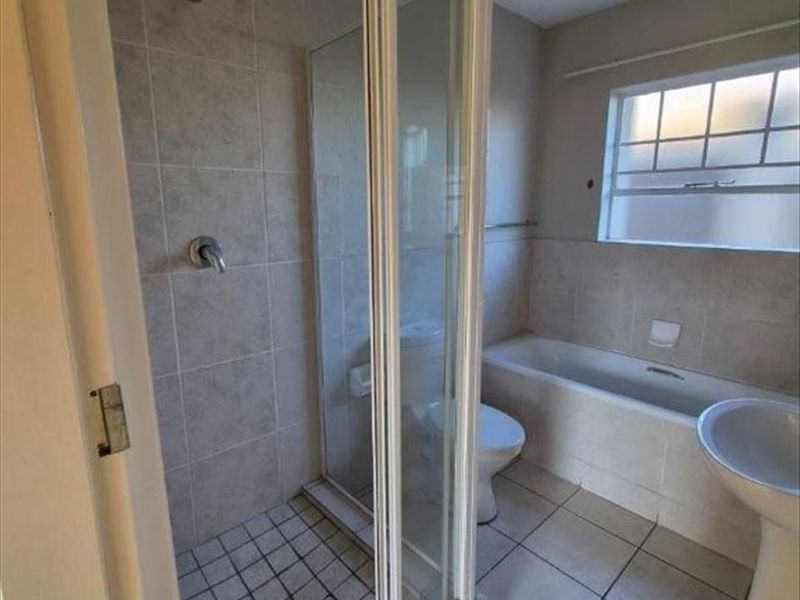A functional bathroom featuring a separate shower enclosure, bathtub, pedestal basin, and toilet with neutral tiled finishes throughout.