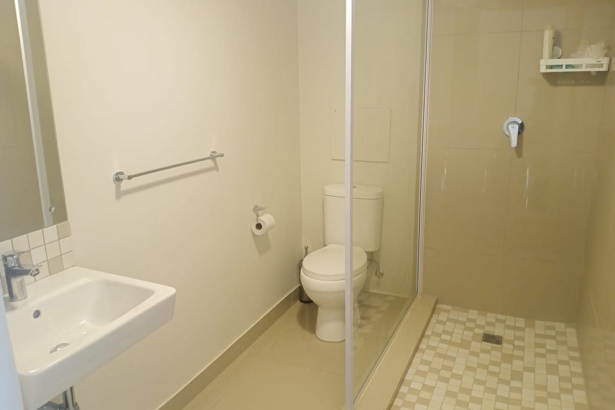 A clean and functional bathroom featuring a walk-in shower with glass screen, wall-mounted basin, and toilet with neutral floor and wall tiling.