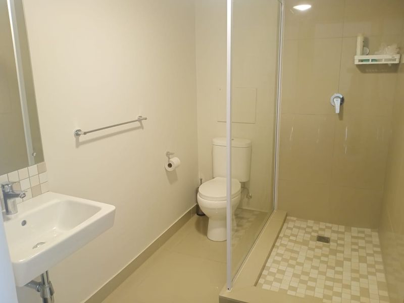 A clean and functional bathroom featuring a walk-in shower with glass screen, wall-mounted basin, and toilet with neutral floor and wall tiling.