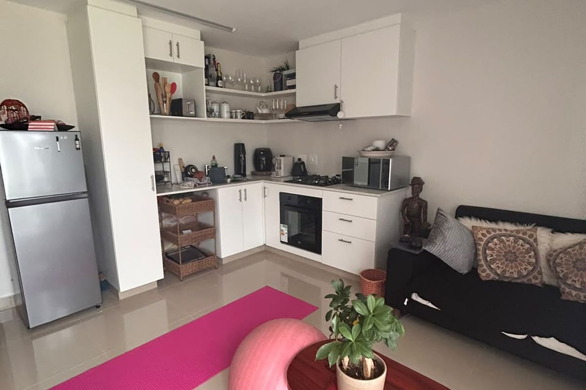 Compact open-plan living area featuring a functional kitchen with white cabinetry, built-in oven, hob, and extractor fan, seamlessly integrated with the living space.