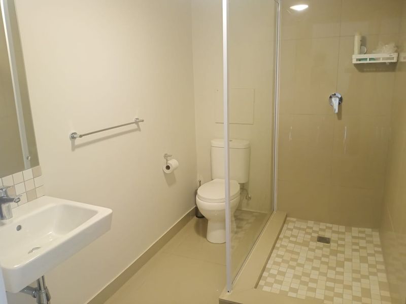 A clean and functional bathroom featuring a walk-in shower with glass screen, wall-mounted basin, and standard toilet with neutral tiling.