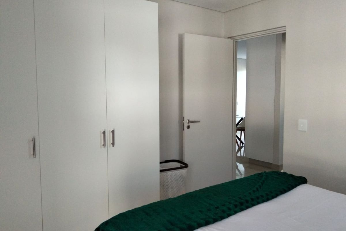 A clean bedroom featuring a white built-in wardrobe and a doorway leading to an adjacent living space.
