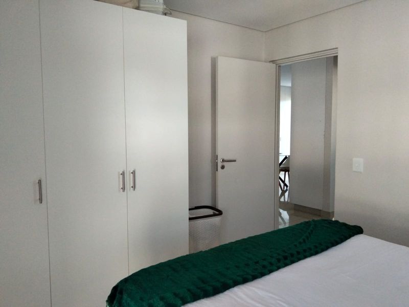 A clean bedroom featuring a white built-in wardrobe and a doorway leading to an adjacent living space.