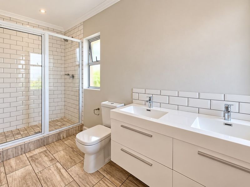 Modern bathroom featuring a double vanity with chrome faucets, a glass-enclosed shower, subway tile accents, and wood-look tiled flooring.