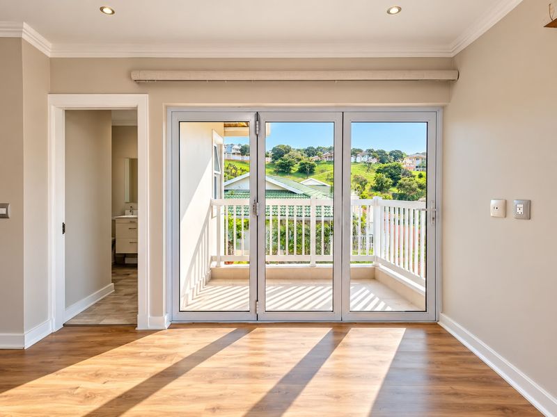 A bright, empty bedroom featuring modern laminate flooring, recessed lighting, and large sliding doors opening onto a private balcony with scenic views.
