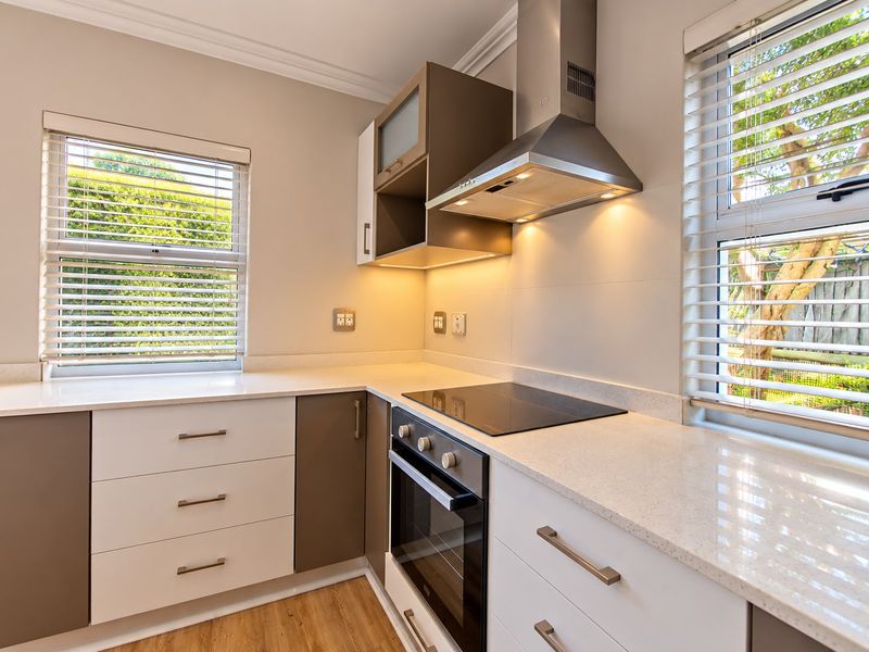 Modern kitchen featuring sleek two-tone cabinetry, stone countertops, integrated electric hob, oven, and extractor fan, complemented by natural light from dual windows.