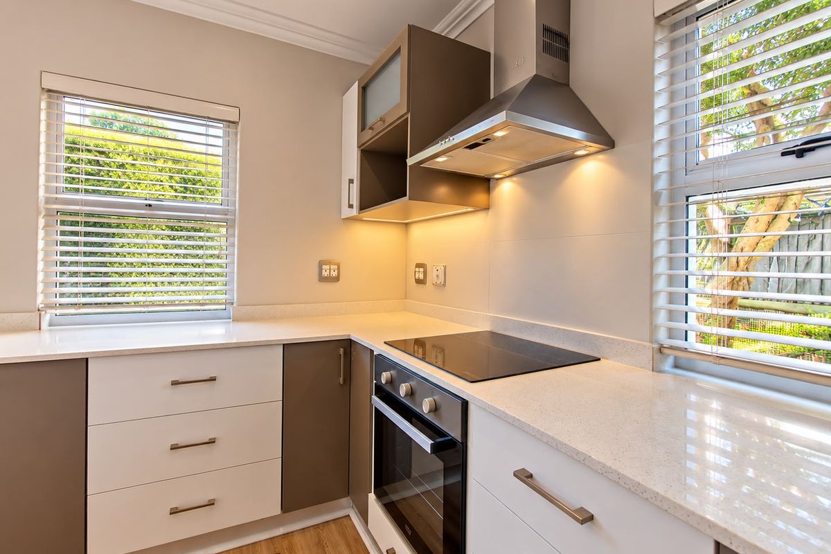 Modern kitchen featuring sleek two-tone cabinetry, stone countertops, integrated electric hob, oven, and extractor fan, complemented by natural light from dual windows.