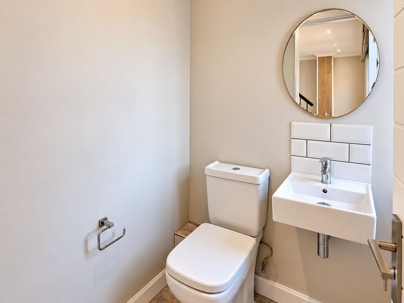 A modern, well-maintained guest powder room featuring a wall-mounted basin, subway tile splashback, and wood-look floor tiles.