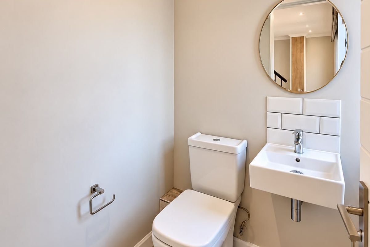 A modern, well-maintained guest powder room featuring a wall-mounted basin, subway tile splashback, and wood-look floor tiles.
