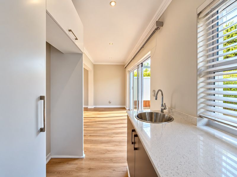 A clean, modern scullery featuring a stainless steel sink, stone countertops, built-in cabinetry, and direct access to the outdoor area through sliding glass doors.