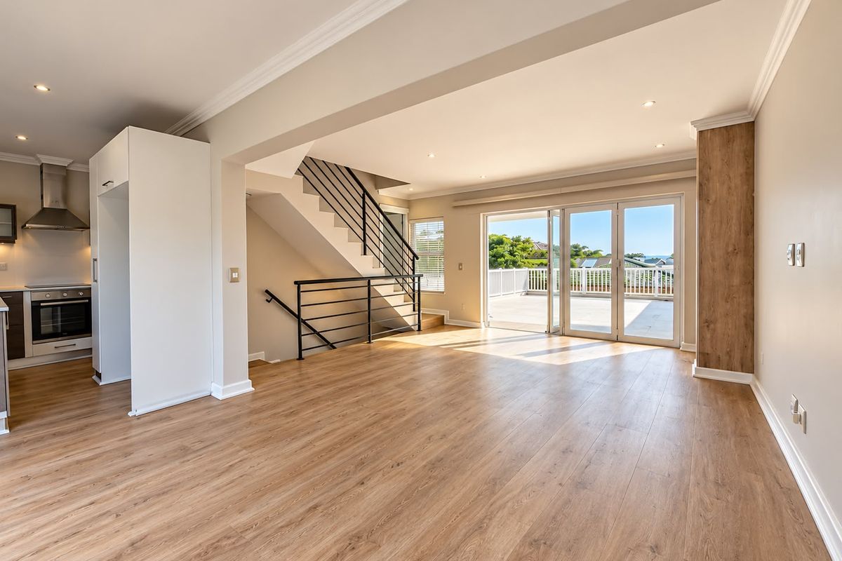 Spacious open-plan living area featuring modern laminate flooring, a sleek staircase, and large sliding doors leading to an outdoor balcony with scenic views.