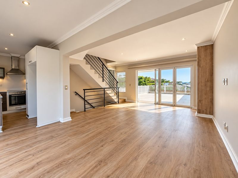 Spacious open-plan living area featuring modern laminate flooring, a sleek staircase, and large sliding doors leading to an outdoor balcony with scenic views.