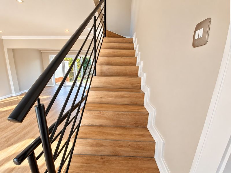 A bright, modern staircase featuring wood-look laminate treads and a sleek black metal balustrade, leading to an open-plan living area.