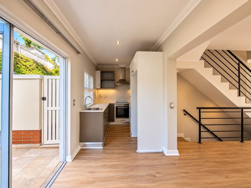 Modern open-plan kitchen area featuring sleek cabinetry, integrated appliances, and laminate flooring, seamlessly connected to an outdoor patio and internal staircase.