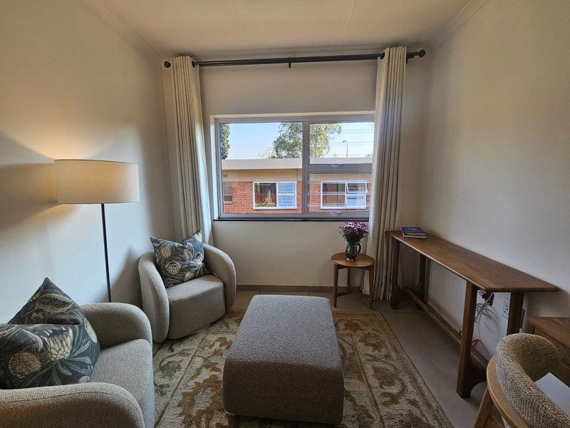 A well-lit living room featuring neutral tiled flooring and a large window with curtain fixtures, providing a comfortable and functional space.