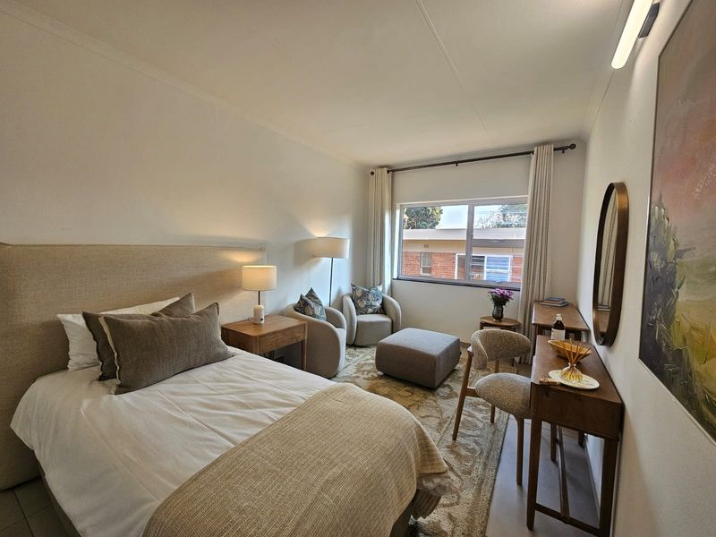 A well-lit, comfortable bedroom featuring neutral tones, tiled flooring, and a large window providing natural light.