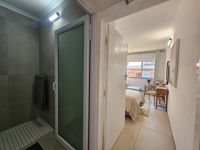 A modern bathroom featuring a walk-in shower with grey tiling, adjacent to a bedroom area with neutral finishes and natural light.