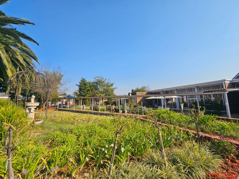 A well-maintained retirement village garden featuring a long covered walkway, established greenery, and an ornamental fountain in a peaceful outdoor setting.