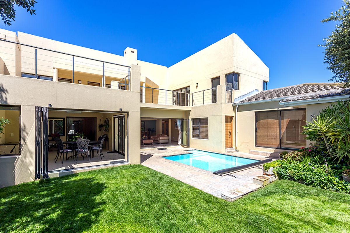 Rear view of a multi-level home featuring a swimming pool, tiled patio area, upper balcony, and seamless indoor-outdoor flow through large glass doors.