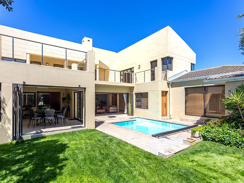 Rear view of a multi-level home featuring a swimming pool, tiled patio area, upper balcony, and seamless indoor-outdoor flow through large glass doors.